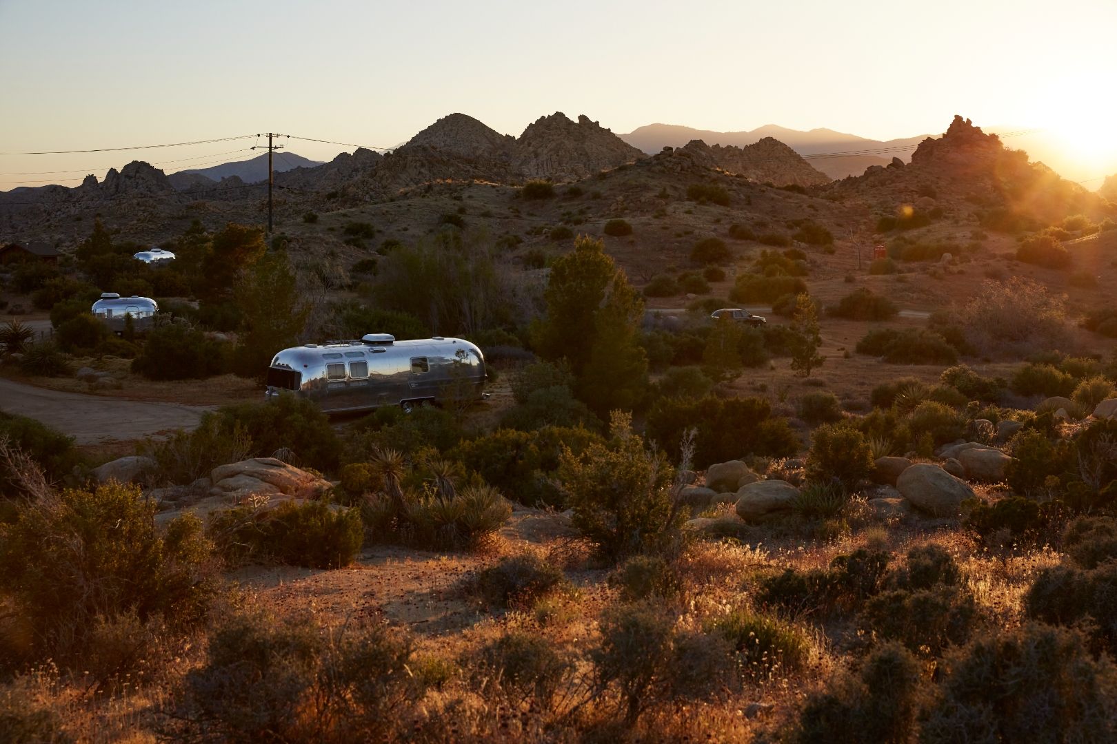 Three Airstreams scattered across the high desert at ESCAPE — sunset over the Pioneertown mountains