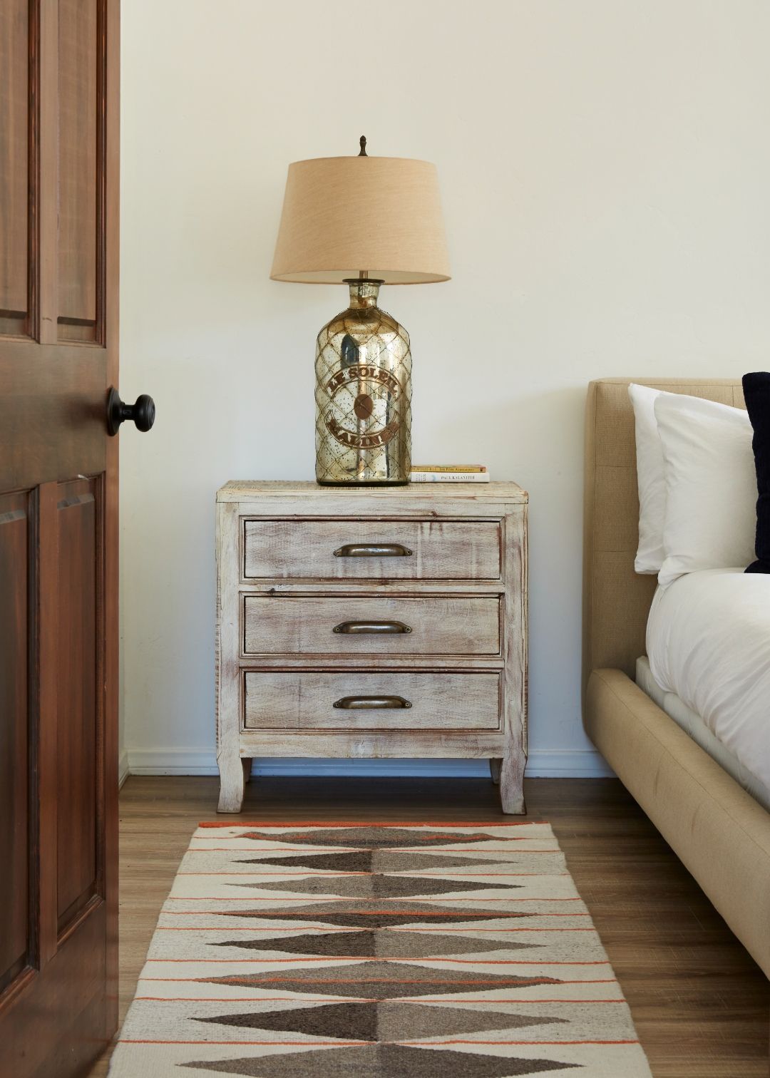 Cottage bedroom detail at ESCAPE — Navajo runner, weathered nightstand, mercury-glass lamp