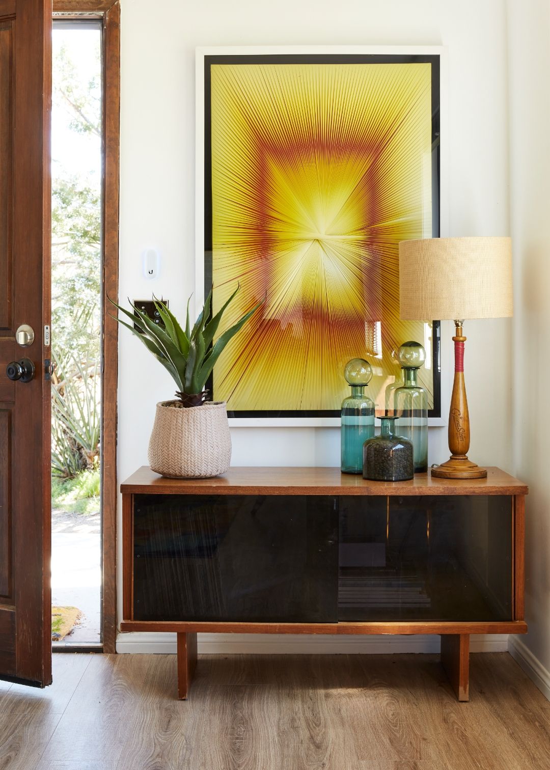 The Cottage entryway at ESCAPE — mid-century console, sunburst artwork, and aloe by the open door
