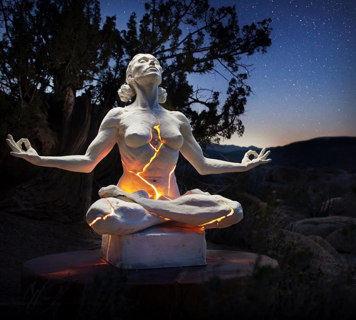 Paige Bradley's Expansion sculpture at ESCAPE — a meditating figure cracked open with light from within, under a starlit desert sky