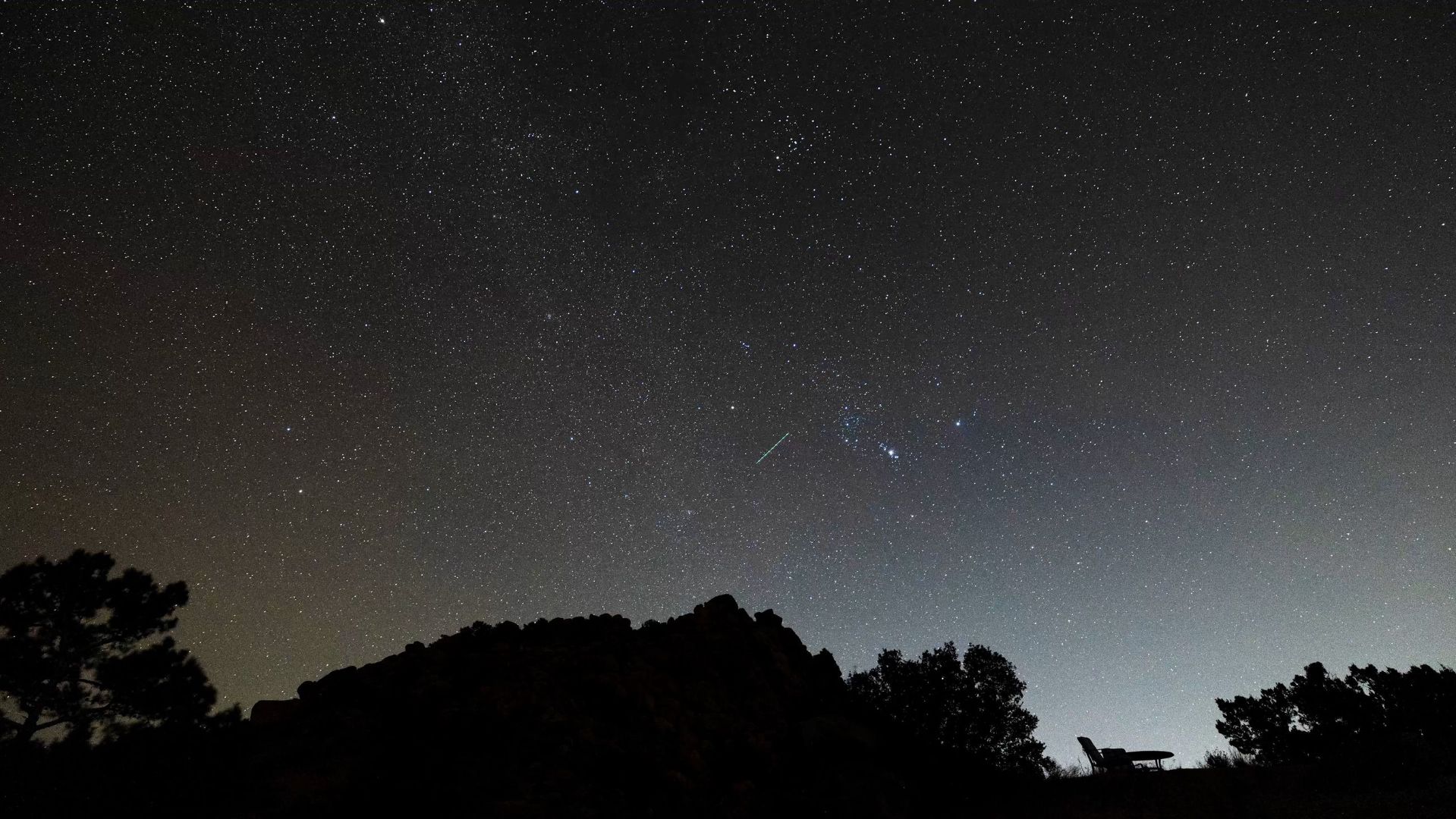 The Milky Way and a meteor over the high desert at ESCAPE, with a lounge chair silhouetted on the ridge